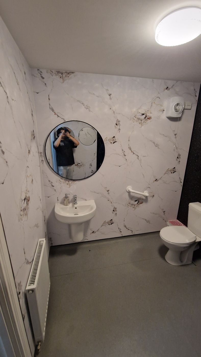 Job E wall 1 after: marble panels behind the basin and toilet, with a round mirror